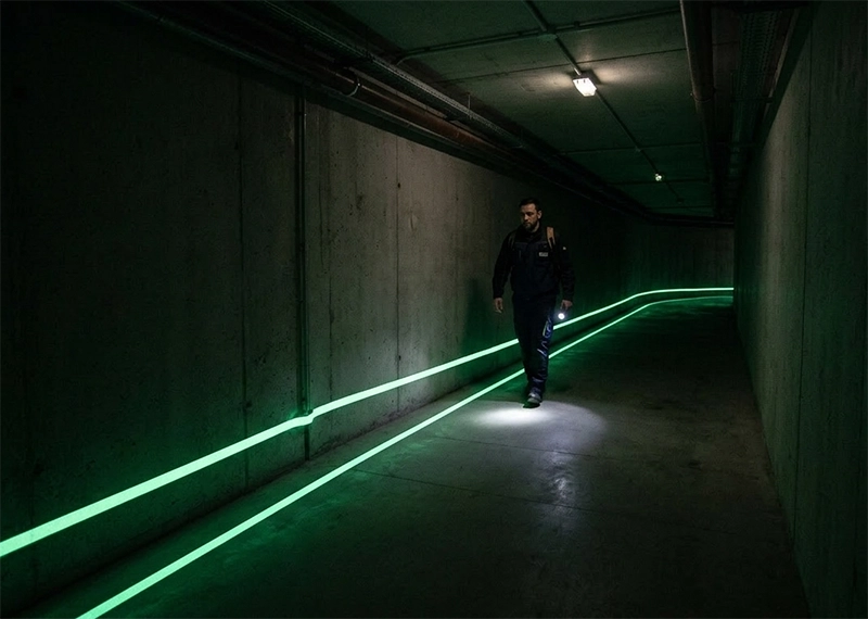 Ligne de guidage photoluminescente en partie basse de couloir d'évacuation avec repérage de l'issue de secours